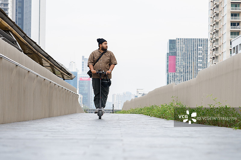 年轻男人沿着城市街道骑电动滑板车图片素材