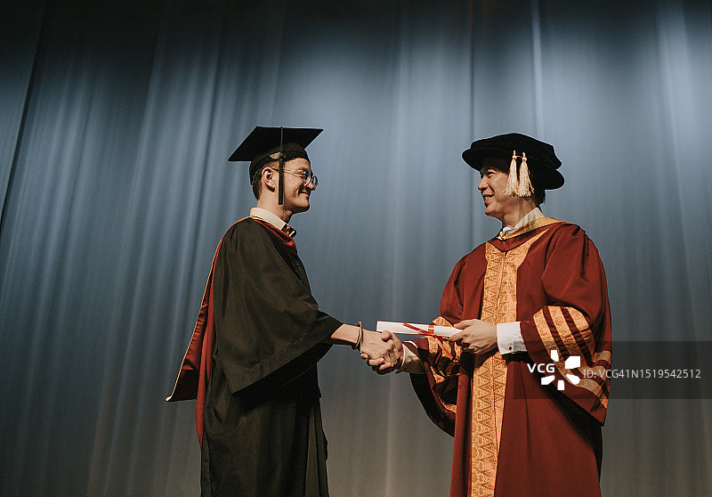 亚洲毕业典礼：大学礼堂内学生与院长握手并获颁证书图片素材