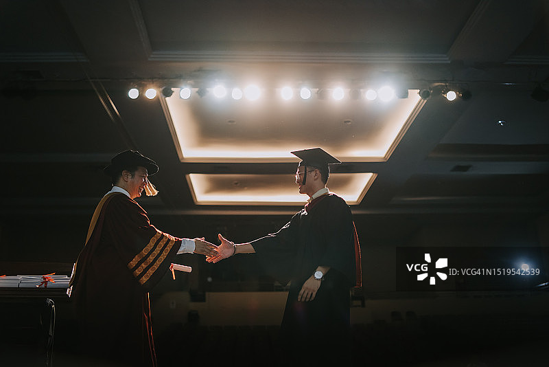 亚洲毕业典礼：大学礼堂内学生与院长握手并获颁证书图片素材