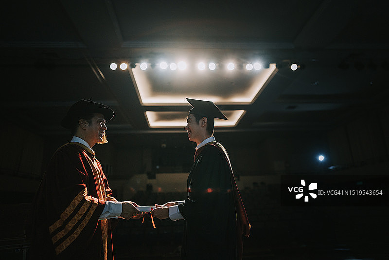 毕业典礼上亚洲院长在礼堂舞台上向大学毕业生颁发毕业证书图片素材