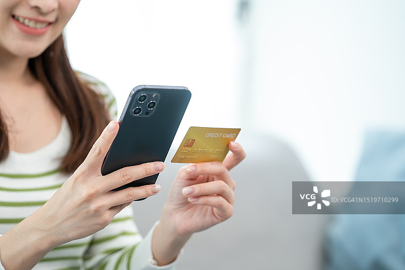亚洲女性在客厅的沙发上拿着信用卡和智能手机，进行在线购物和在线支付图片素材