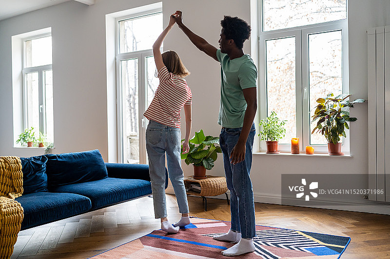 在客厅里跳舞，随着音乐移动的年轻多元化家庭夫妇图片素材