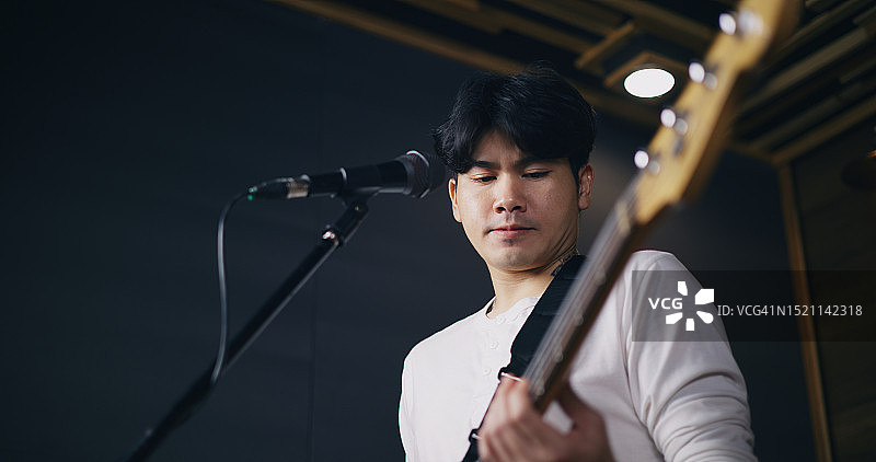 在灯光照亮的排练室里，穿着休闲服装的年轻亚洲男音乐家演奏电吉他图片素材