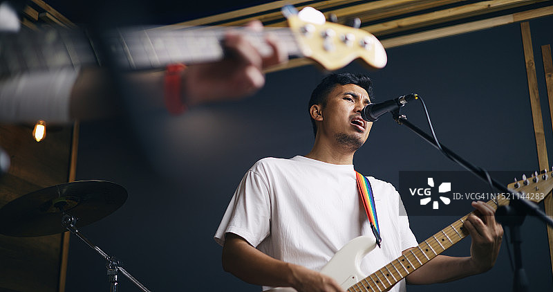 年轻的亚洲男性音乐家穿着休闲服装，弹着电吉他，同时歌手在唱歌图片素材