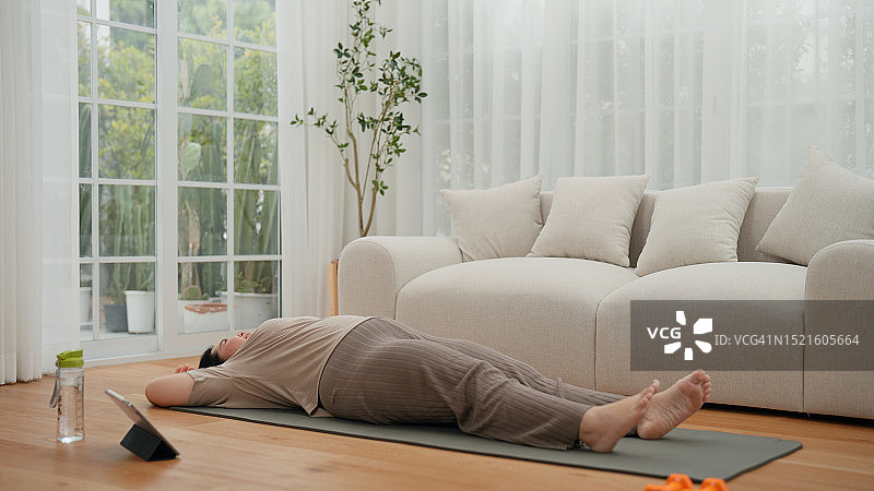 亚洲年轻肥胖女性坐在瑜伽垫上休息，完成客厅仰卧起坐练习图片素材
