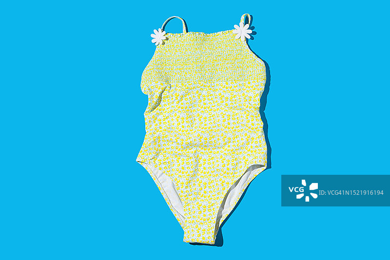 柠檬黄色女士泳衣，蓝色背景下的硬阴影，夏季海滩泳池概念图片素材