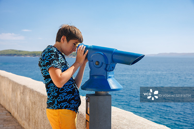 站在海边墙边用双筒望远镜观看的少年图片素材