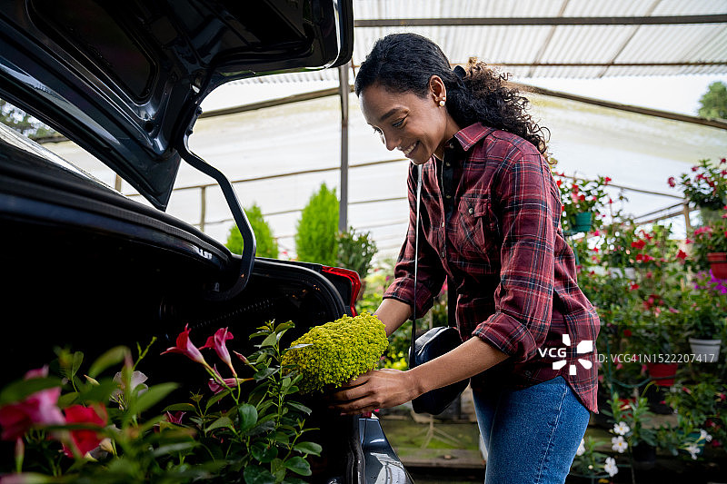 在植物苗圃购买植物并将其装入汽车的快乐女人图片素材