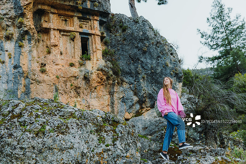 身穿粉色毛衣，背着背包，探索土耳其森林中古城遗址的女人图片素材