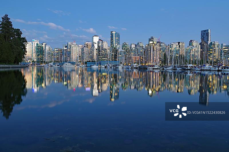 平静水面映衬着灯火辉煌的摩天大楼，黄昏，加拿大不列颠哥伦比亚省温哥华市中心斯坦利公园图片素材