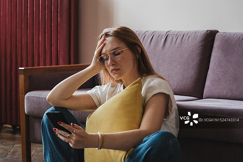 沮丧的红发女孩拿着智能手机，阅读短信，收到不愉快的坏消息，社交媒体使用与抑郁图片素材
