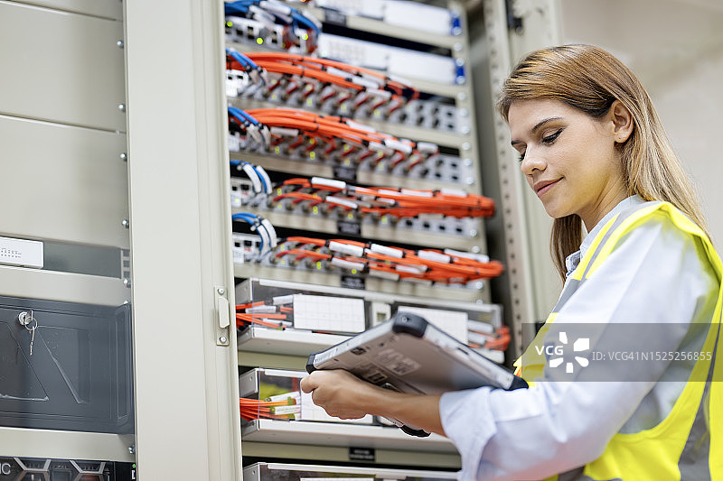 数据中心解决方案提升业务运营效率和数据保护。一名女网络工程师使用平板电脑在服务器机房中进行故障排除和网络性能监控。图片素材