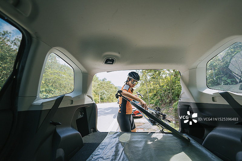 华人女自行车手在乡村的SUV后备箱中放置自行车图片素材
