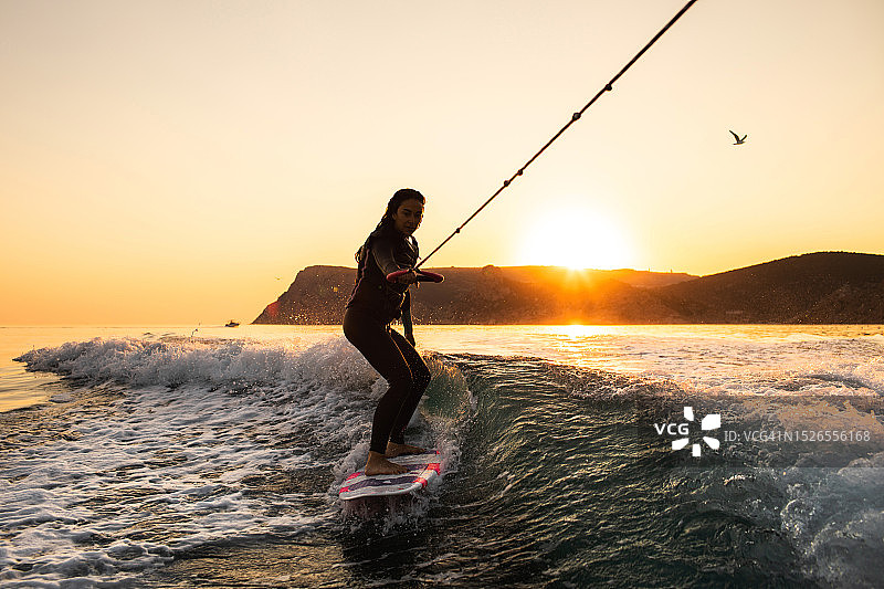 女人正在学习在船后的海面上玩尾波冲浪图片素材