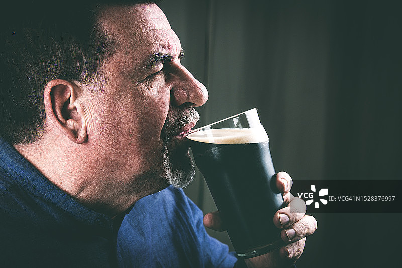 男人从玻璃杯里喝黑啤酒图片素材