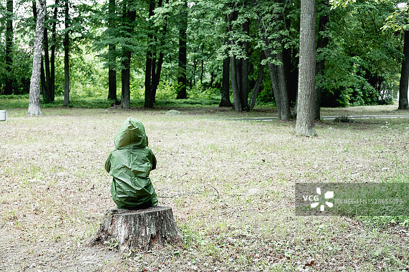 穿绿色带帽雨衣的女孩坐在森林空地树桩上图片素材