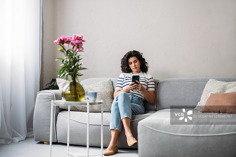 坐在沙发上，用智能手机浏览社交媒体的年长的白人妇女图片素材
