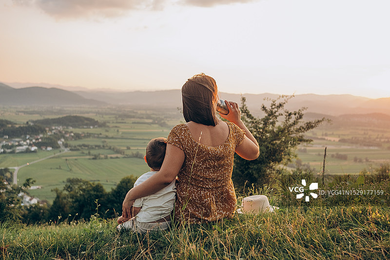 夕阳下，妈妈在山顶拥抱儿子并喝着热饮图片素材