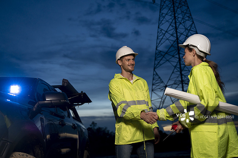 电力塔前握手的工程合作者图片素材
