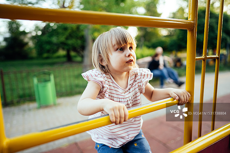 小女孩在夏季操场上攀爬攀登架图片素材