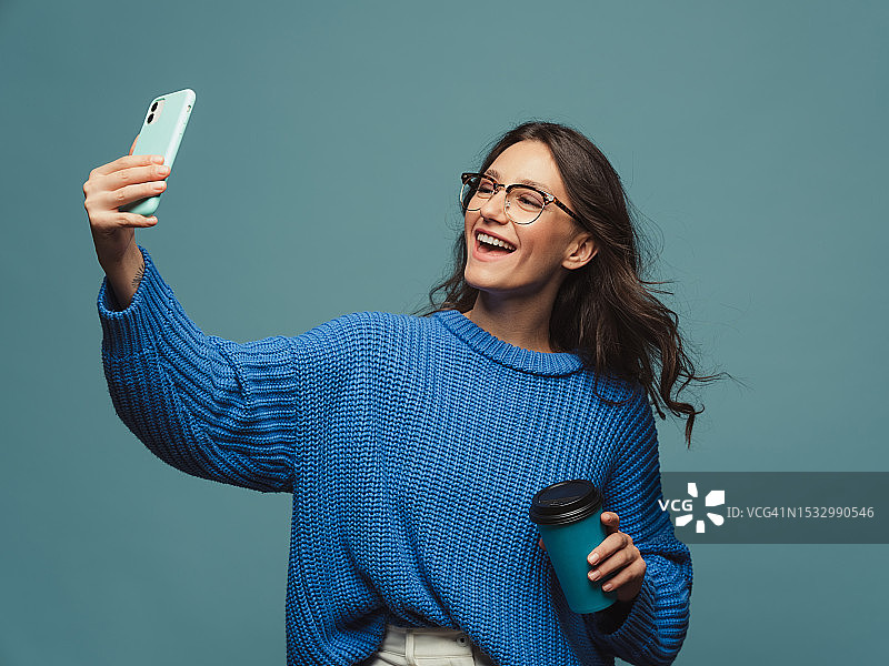 穿着蓝色毛衣、手捧咖啡杯用手机的女人肖像图片素材