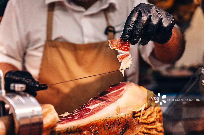 男人在肉店用刀切伊比利亚火腿片图片素材