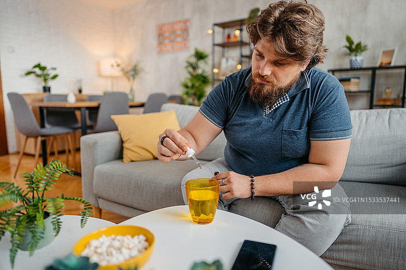 年轻男人将药滴滴入一杯水中图片素材