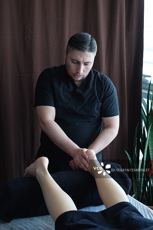 医生、理疗师用手进行生理治疗。按摩师、脊椎指压治疗师为患者进行治疗性按摩，缓解肌肉痉挛和腿部疼痛。整骨疗法。替代医学。图片素材