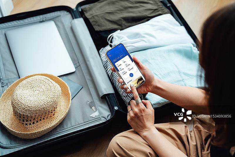 年轻女子用手机预订度假航班（肩上视角）图片素材