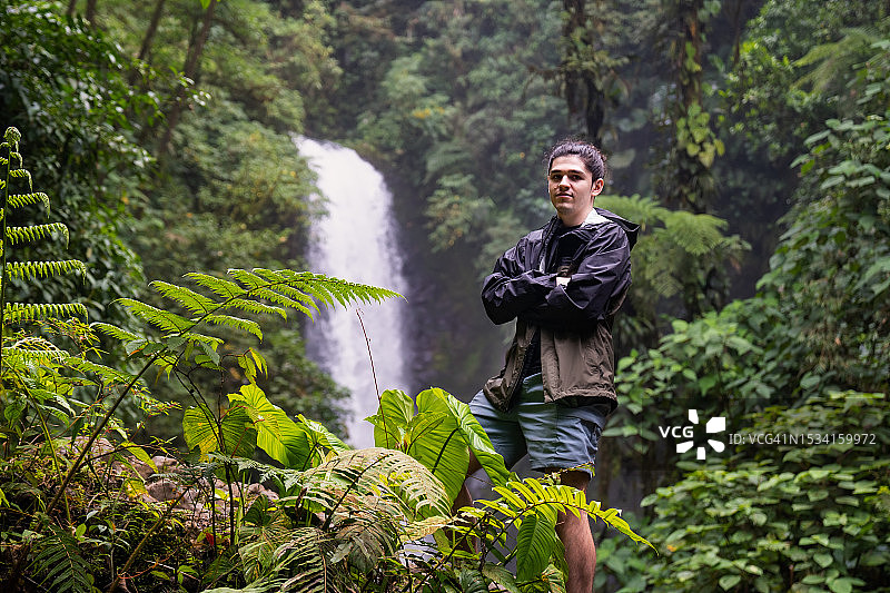 年轻男子站在雨林瀑布前的肖像图片素材