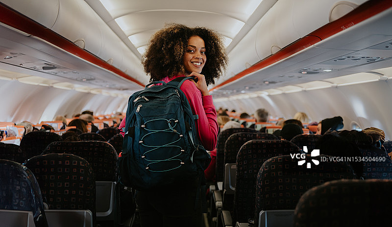 一名妇女携带手提行李登上商用飞机，她回头对着镜头微笑图片素材