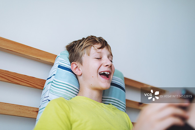 学龄男孩在家躺在床上用手机玩视频游戏图片素材