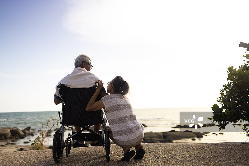 坐在轮椅上的年长男人和坐在他旁边的年长女人看着海景图片素材