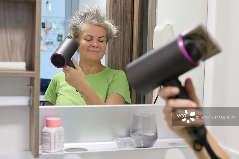 在前面吹干头发的成熟灰发妇女图片素材