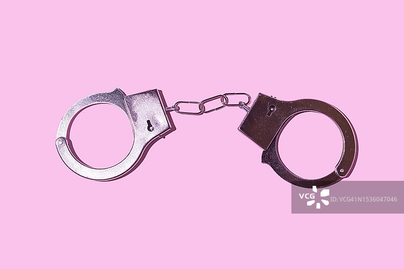 粉红色背景上的闭合金属手铐。警察、监狱、囚犯、非法、抢劫、法律、审判和小偷概念。图片素材