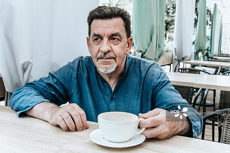 一位老人在街边咖啡馆的桌旁用杯子喝咖啡图片素材