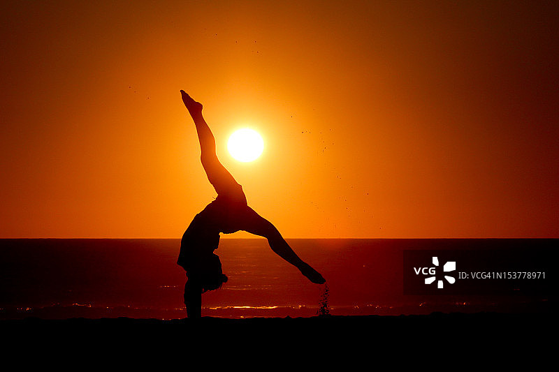 日落时分在海滩上手倒立的体操女孩图片素材