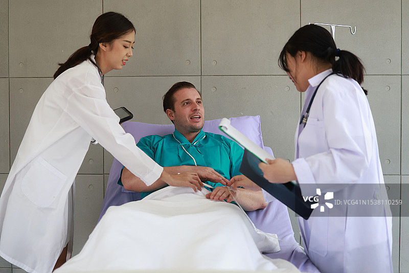 医生和实习医生与他们的病人交谈。医疗专家支持躺在医院病床上与他们交谈的病人。健康检查、咨询、治疗概念图片素材