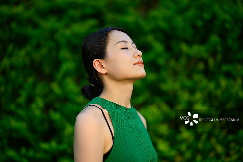 年轻的亚洲女商人站在城市办公园区内思考，周围是绿色植物，生态户外，可持续生活方式概念图片素材