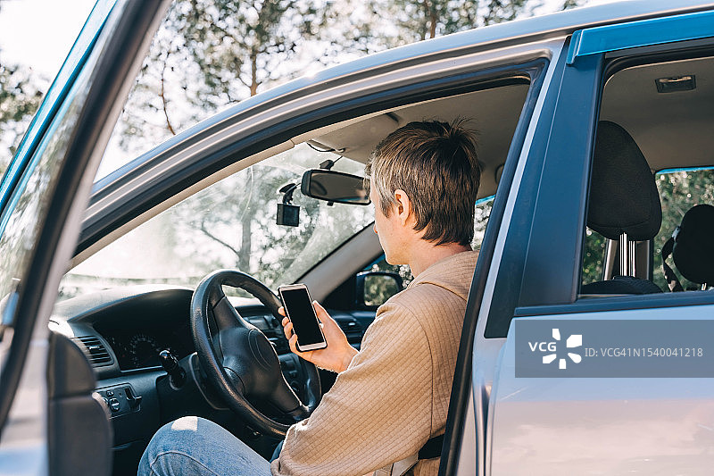 阳光明媚，年轻男子坐在车里，在手机上的导航仪上规划路线图片素材