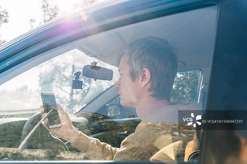 阳光明媚，年轻男子坐在车里，在手机上的导航仪上规划路线图片素材