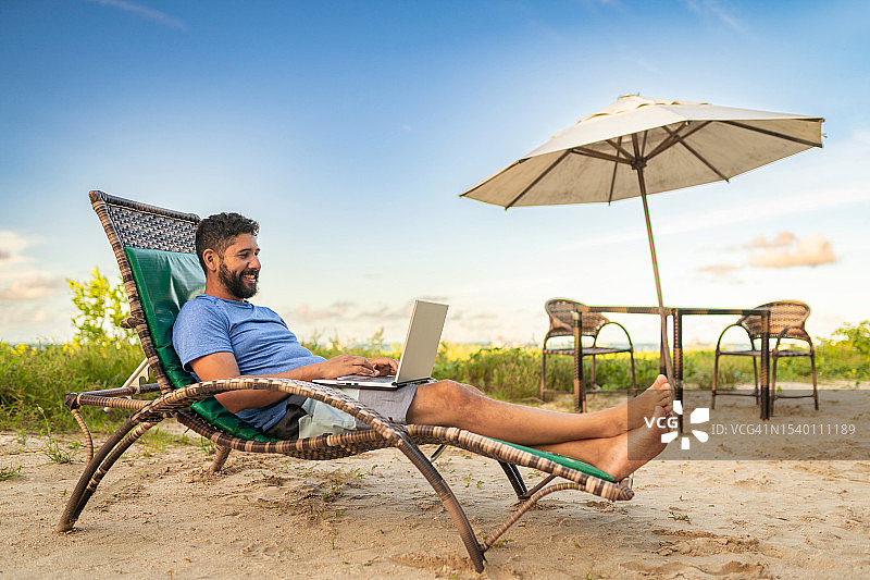男人在海滩度假时使用笔记本电脑图片素材