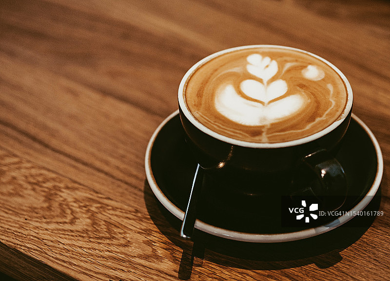 木桌上带有奶泡图案的黑色卡布奇诺咖啡（顶视图）图片素材