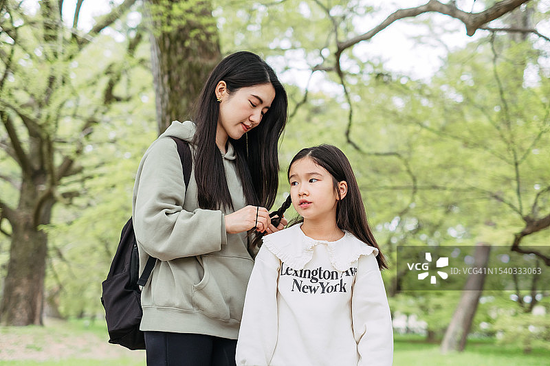 在京都，日本，年轻的亚洲母亲帮助女儿在公园里扎头发图片素材