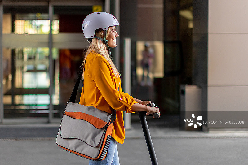 30多岁戴着头盔穿着黄色外套骑着电动车回家的年轻微笑女子图片素材