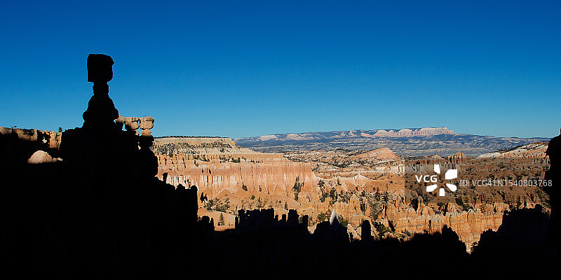 坐在岩石上，以布莱斯峡谷国家公园的湛蓝天空为背景的男子轮廓，美国犹他州图片素材