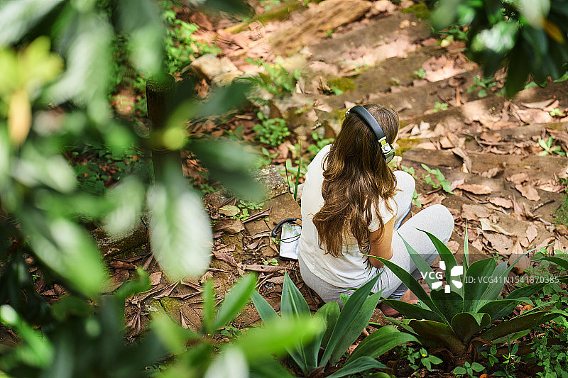女子独自坐在森林里戴着耳机听音乐图片素材