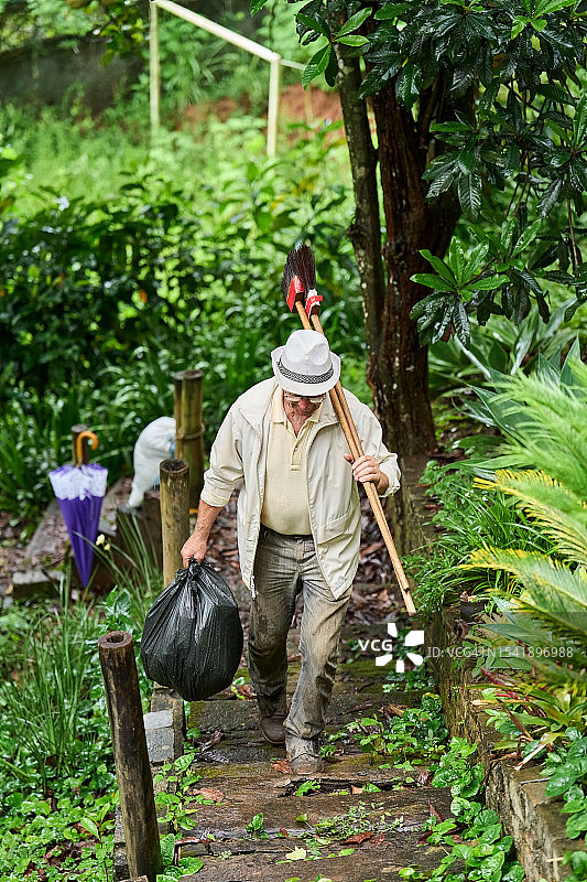 年长的男人在花园里拿着垃圾袋和扫帚参加社区清洁日活动图片素材