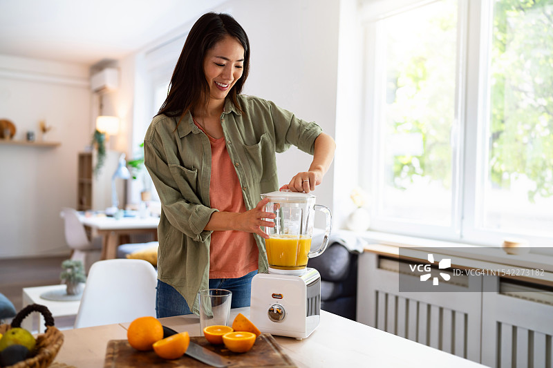 女人在家用搅拌机制作新鲜橙汁图片素材