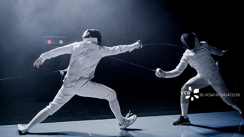 两位职业击剑手用花剑进行决斗，舞台灯光为蓝色，有烟雾效果图片素材